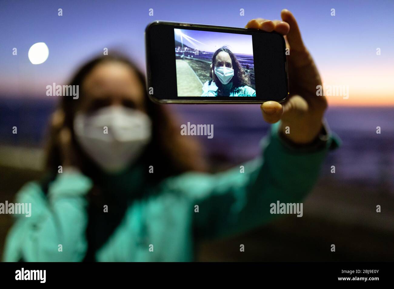 Donna caucasica che indossa una maschera protettiva contro il coronavirus, scattando una foto per le strade Foto Stock