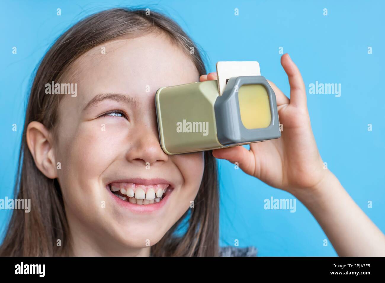 Sorridente bambina guarda vecchie foto attraverso un diascope. Modello banner su bg blu. Foto Stock