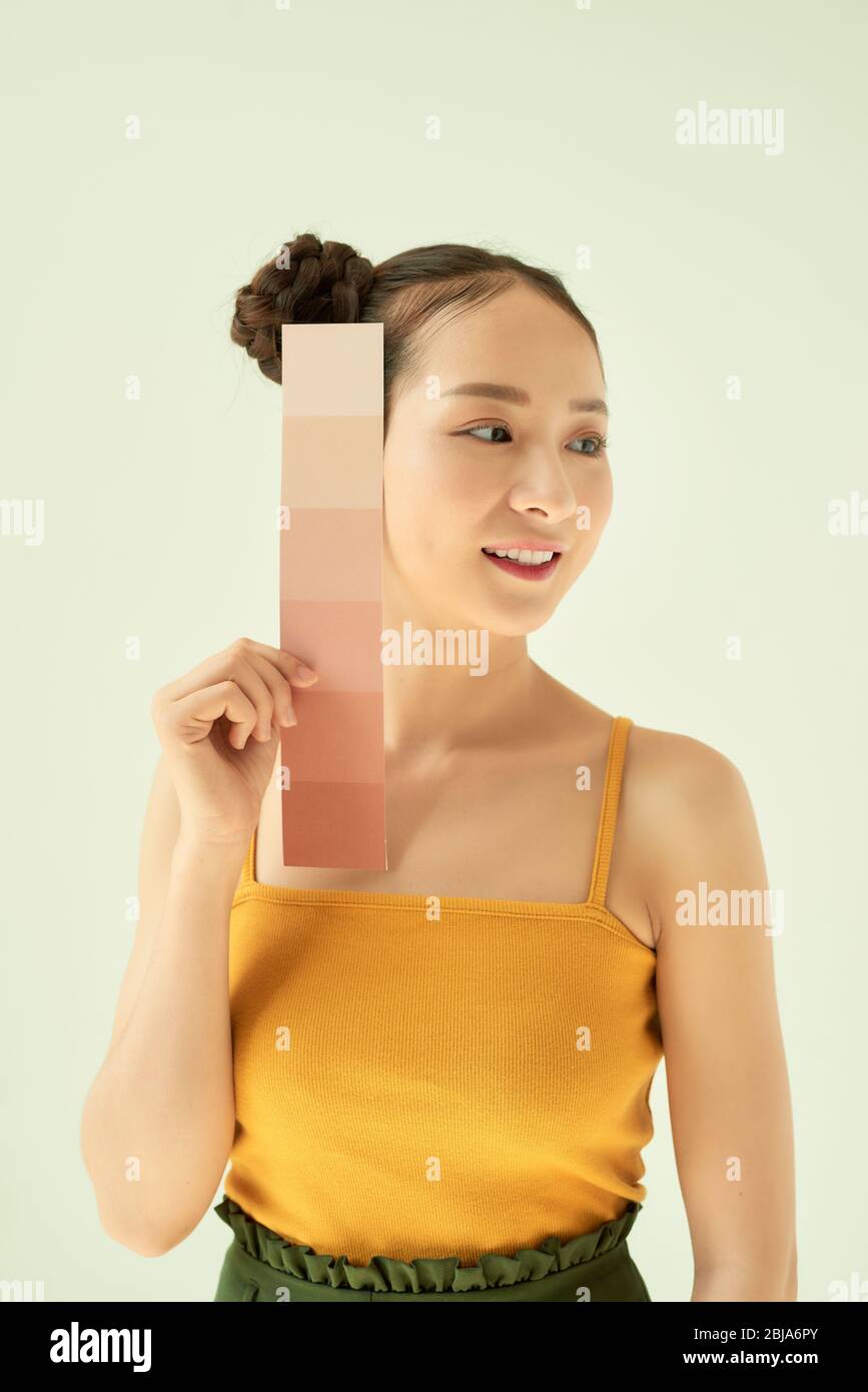 Giovane donna sorridente con tavolozza dei toni della pelle o campioni mentre si levano in piedi su sfondo chiaro Foto Stock