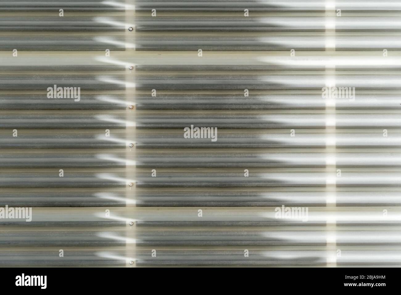 Ombra e luce formano modelli astratti lineari e freccia, mentre la luce del sole colpisce il rivestimento esterno di plastica su una parete in Australia Foto Stock