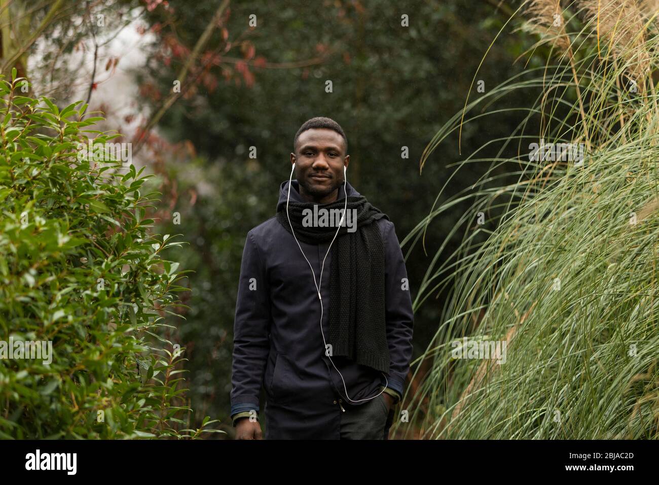 Giovane uomo con auricolari in posa nel parco Foto Stock