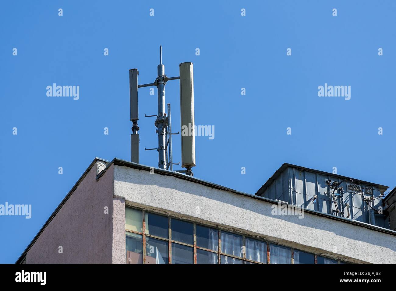 Antenna di comunicazione cellulare su un tetto piatto di un edificio di appartamenti a più piani contro il cielo blu in una giornata di sole. Vista ad angolo basso. Foto Stock
