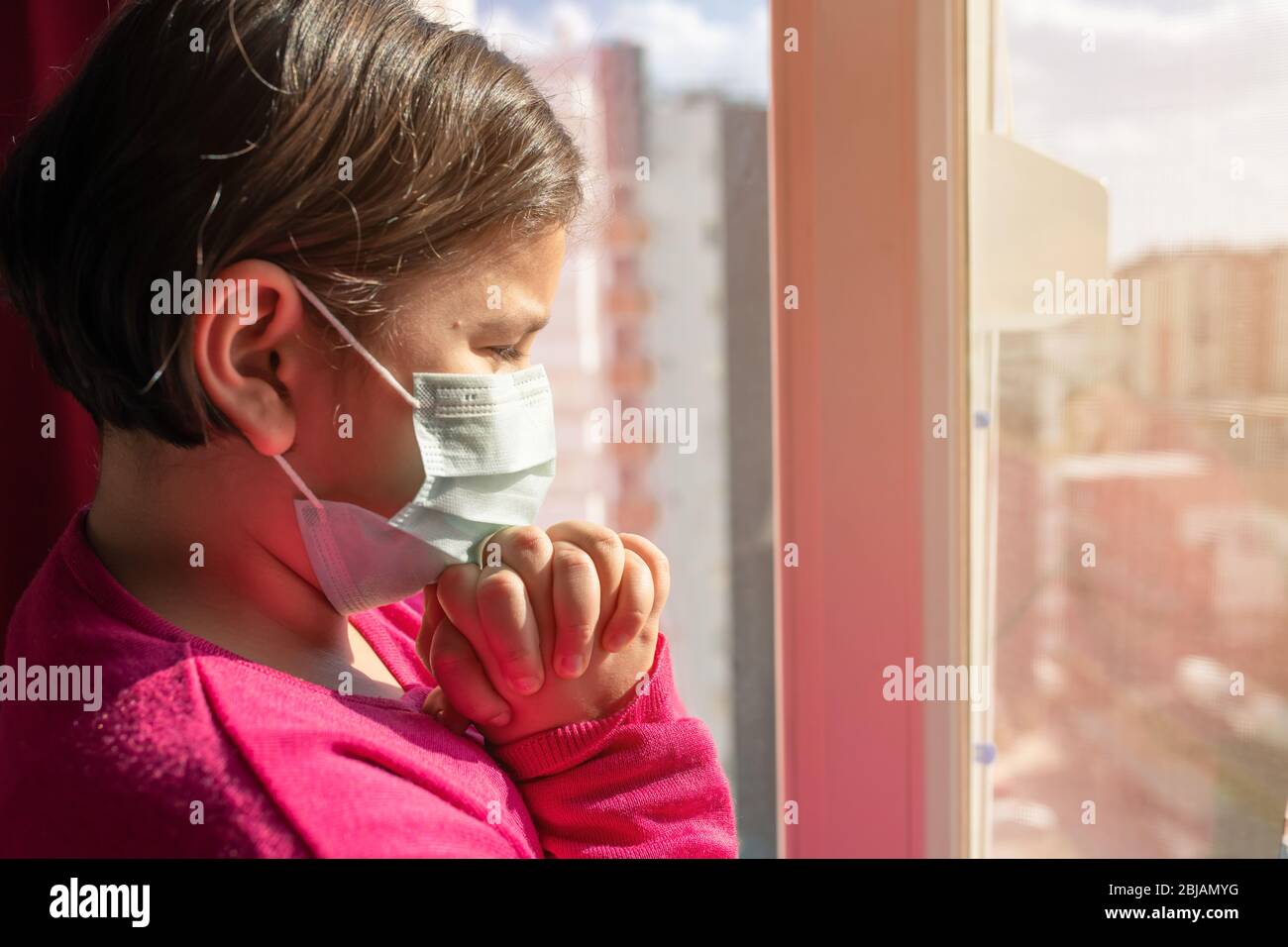 Bambina con maschera che prega per il passaggio del coronavirus Covid-19. Bambina prega di mano per Dio. Foto Stock