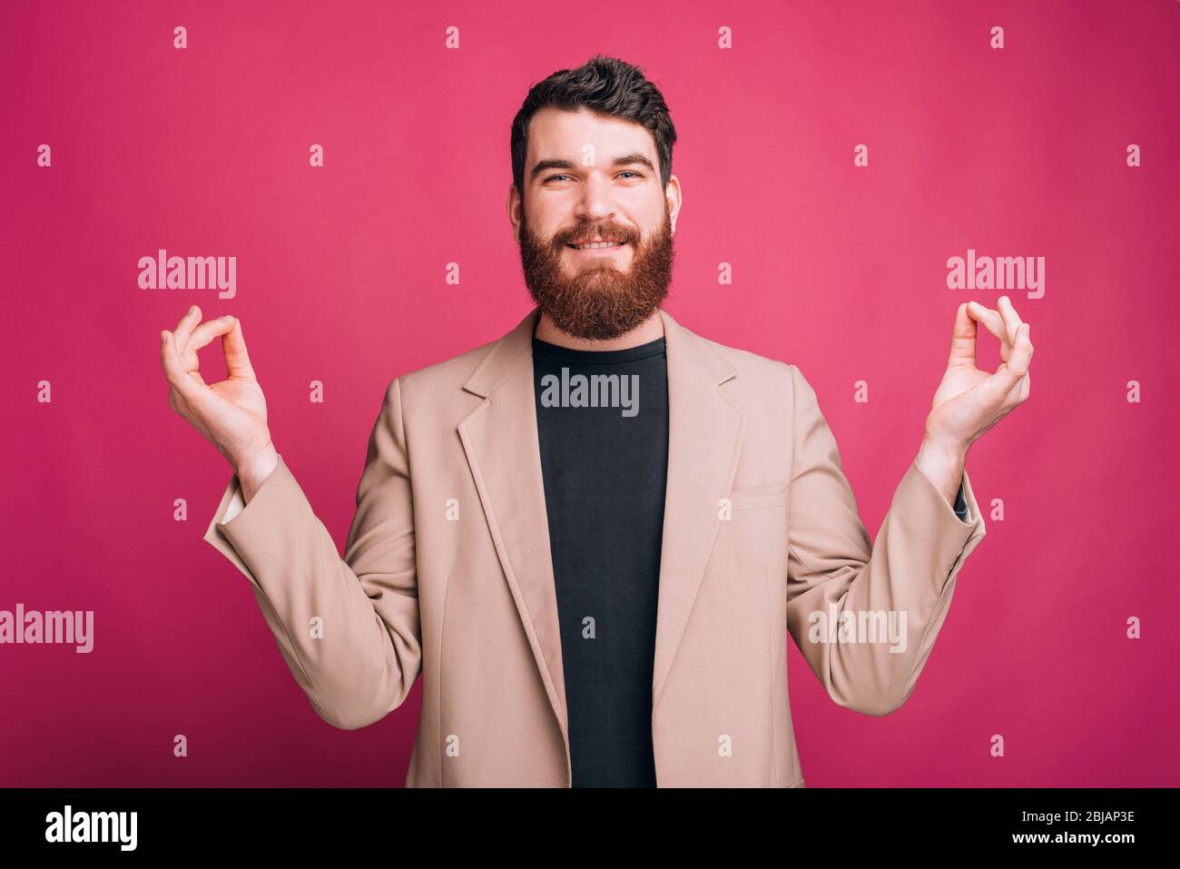 Giovane uomo bearded è in piedi in posa zen guardando la telecamera su sfondo rosa. Foto Stock