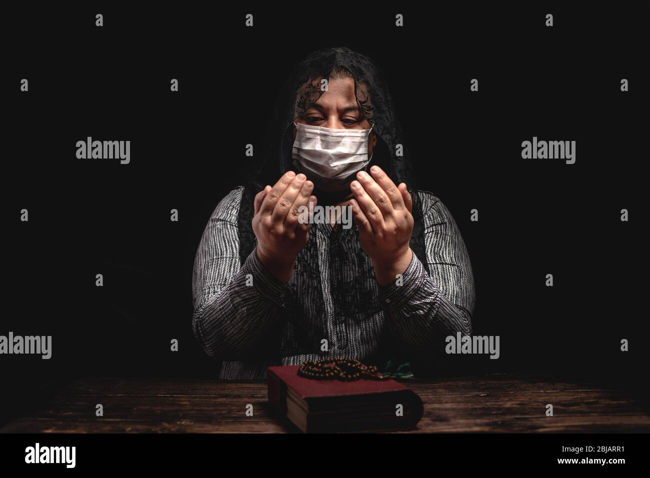 Donna che tiene rosario su libro santo che rimane a casa e che prega per protezione ageainst coronavirus covid-19 pandemi concetto. Foto Stock