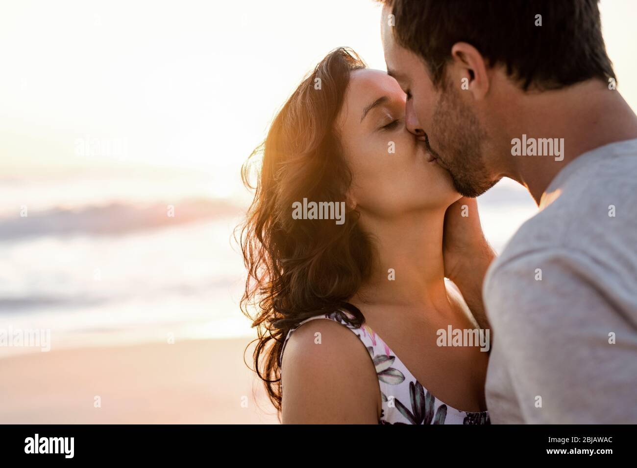 Una giovane coppia che ama baciare su una spiaggia al tramonto Foto Stock