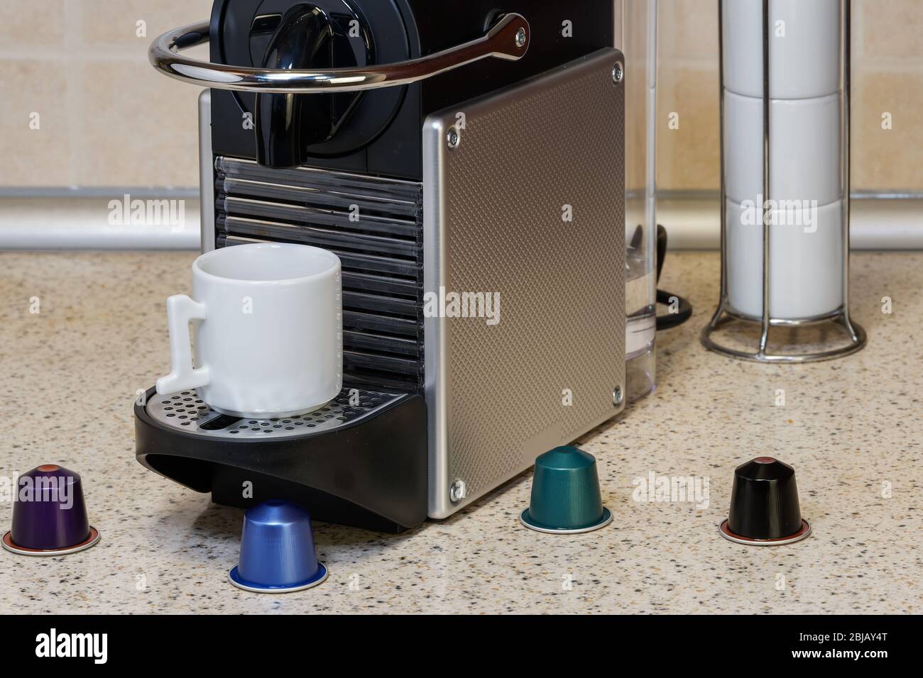 Creazione di espresso su macchina automatica con capsule di alluminio. Cialde colorate in metallo intorno alla macchina per il caffè e una tazza bianca, per preparare caffè caldo gocciolante. Foto Stock
