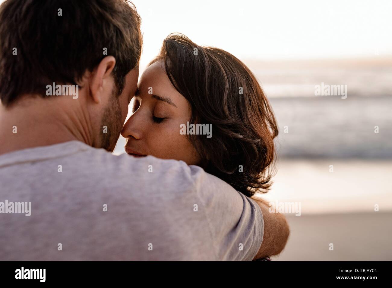 Donna amorevole in piedi tra le braccia del marito su una spiaggia Foto Stock