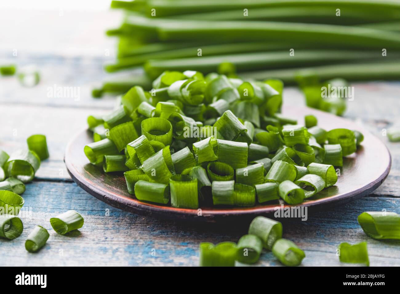 Cipolla fresca verde tritata e si trova su una ciotola su uno sfondo di pannelli blu. Erba cipollina ha molte vitamine e minerali. Foto Stock