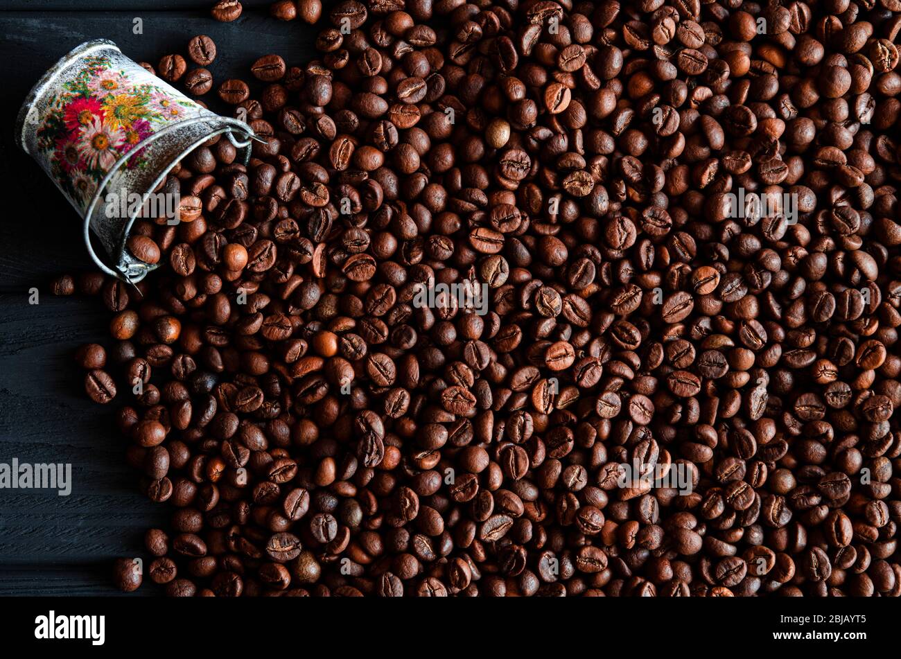 Chicchi fritti di fragrante caffè fresco sparsi da un secchio su un tavolo di legno Foto Stock