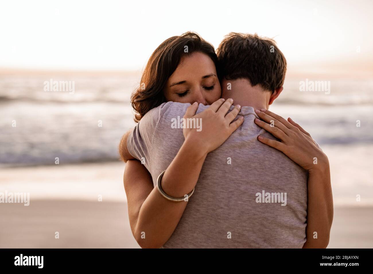 Donna amorevole che abbracciano suo marito su una spiaggia al crepuscolo Foto Stock