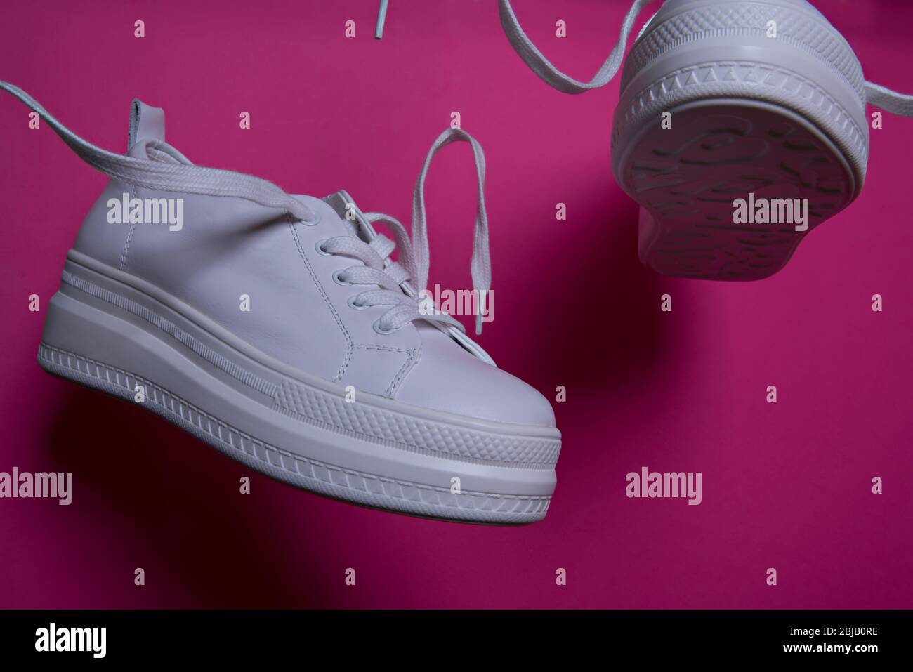 Sneaker bianche in aria su sfondo rosa. Surrealismo astratto e minimalismo concetto di shopping. Foto Stock