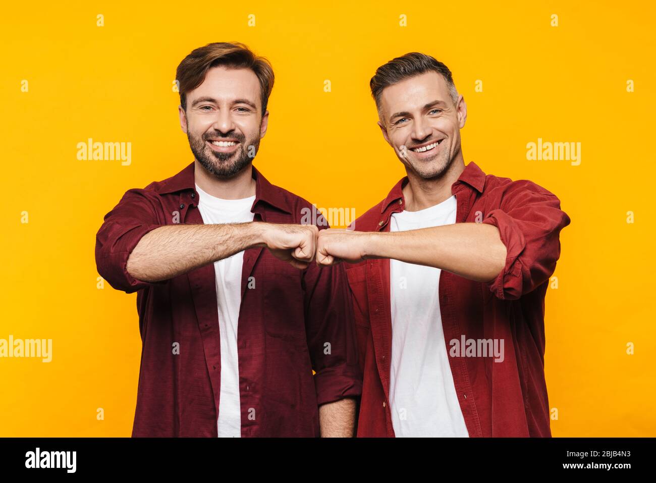 Immagine di due bei uomini 30s in camicie rosse sorridenti e urtare i loro pugni isolati su sfondo giallo Foto Stock