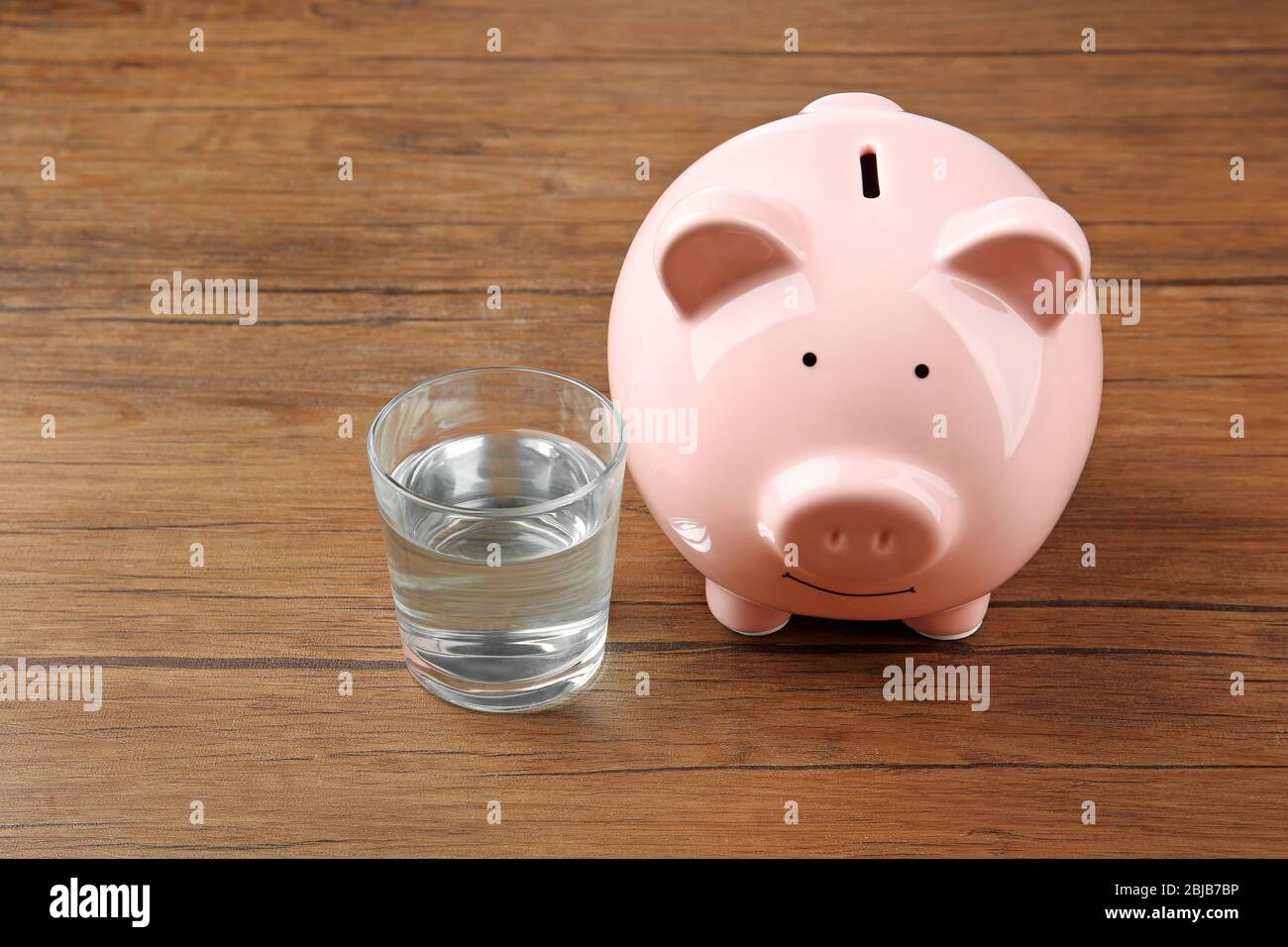 Bicchiere di acqua e scatola di maiale su sfondo di legno Foto Stock