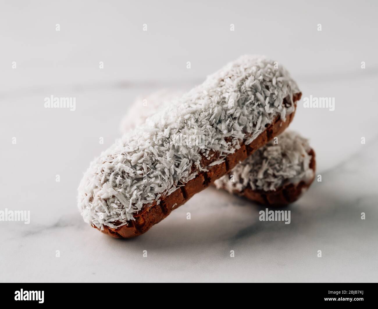 Eclairs fatti in casa con cocco su sfondo di marmo bianco. Da vicino si può ammirare un delizioso e salutare profittato di cocco grattugiato. Spazio di copia per testo o disegno. Foto Stock