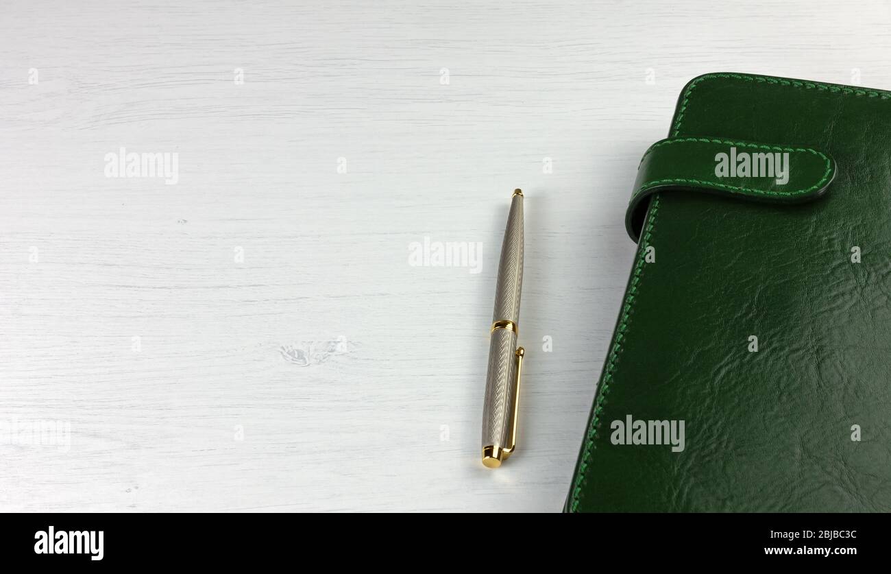 Elegante penna e pianificatore giornaliero con una copertina in pelle verde su una scrivania in legno bianco Foto Stock