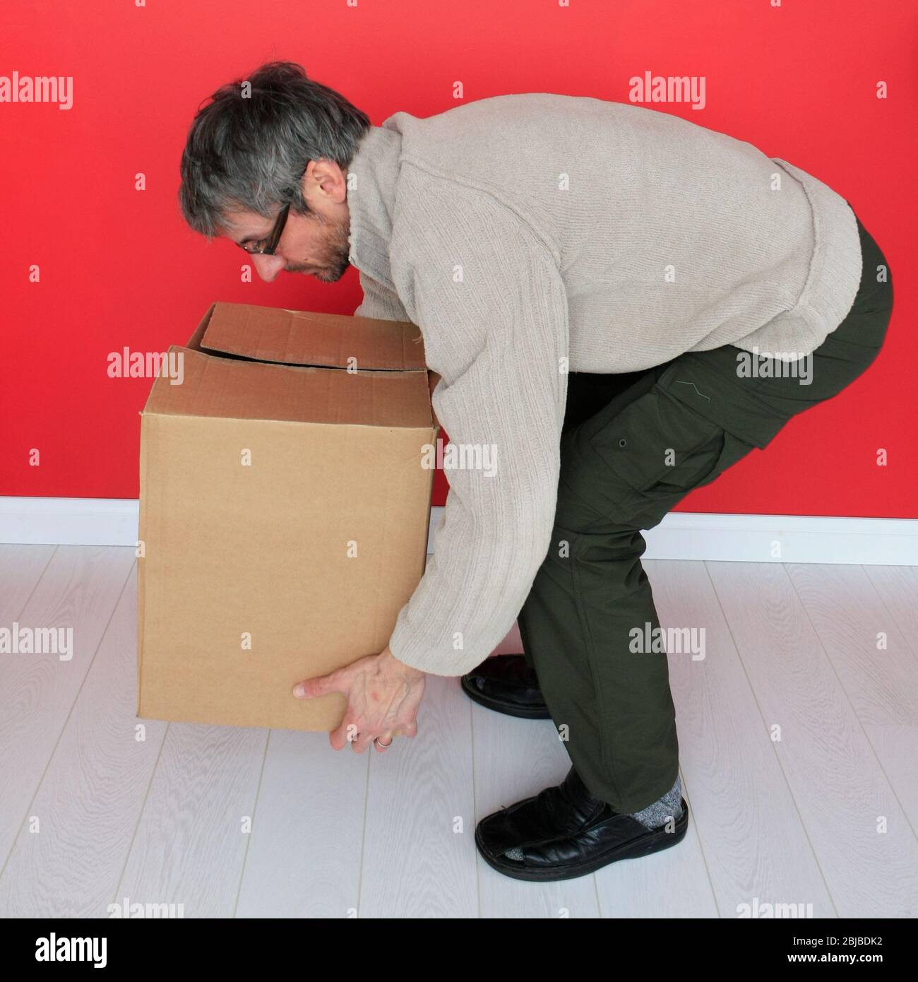 Maschio piegando le ginocchia per sollevare una scatola pesante Foto Stock