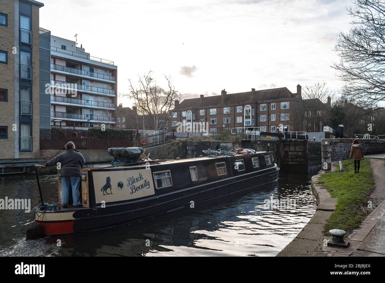 Un uomo che guida una casa galleggiante verso un blocco sul canale del Regent a Londra Est in inverno Foto Stock