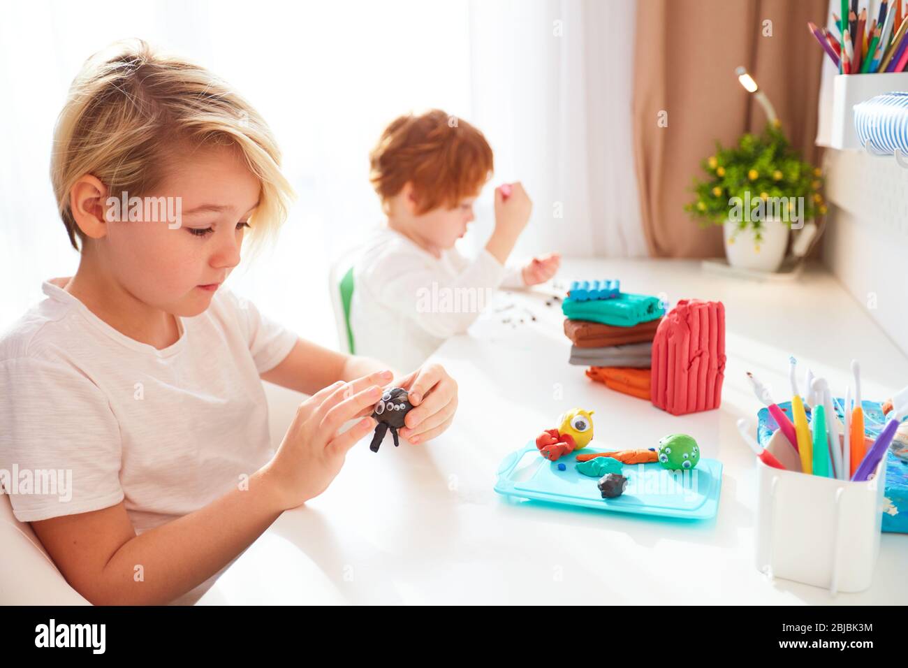 i bambini carini stanno creando i mestieri della mano dalla plastilina di modellizzazione alla stanza dei bambini Foto Stock