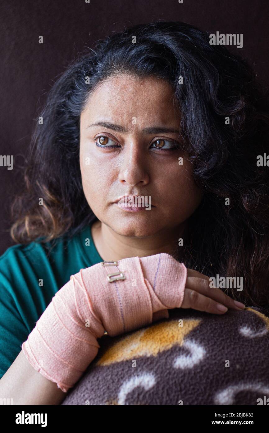 Donna indiana con il polso rotto che si recupera nel letto dell'ospedale guardando lontano dalla macchina fotografica Foto Stock