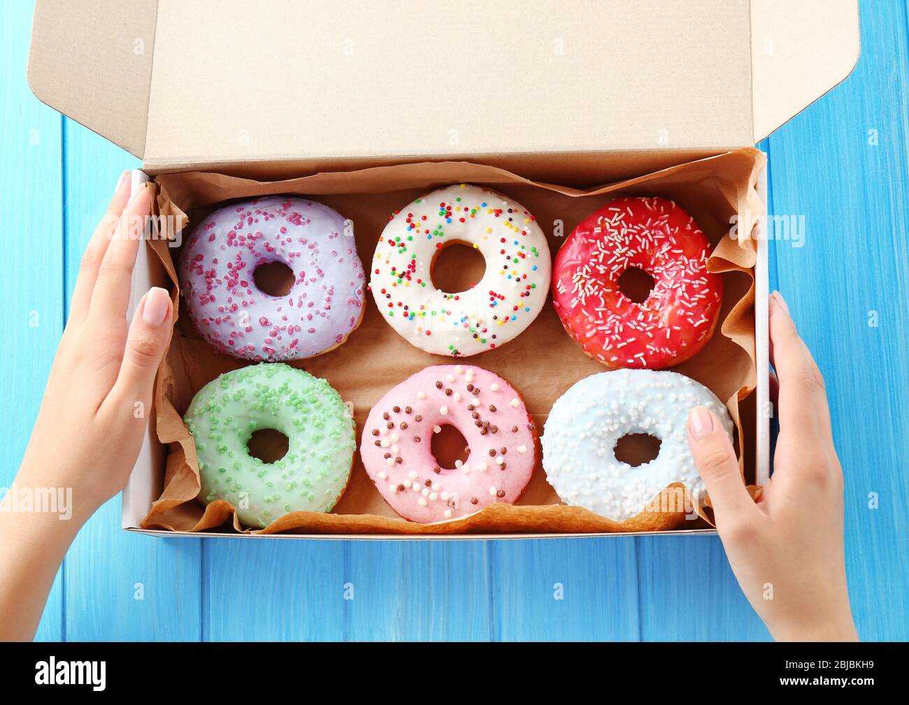 Scatola per mani femminili con ciambelle colorate su sfondo di legno blu Foto Stock