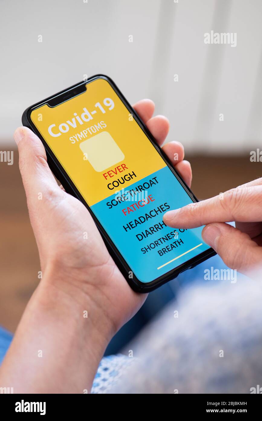 primo piano di un giovane caucasico, seduto comodamente in poltrona, controllando alcuni dei sintomi del covid-19 in una app simulata nel suo smartpho Foto Stock