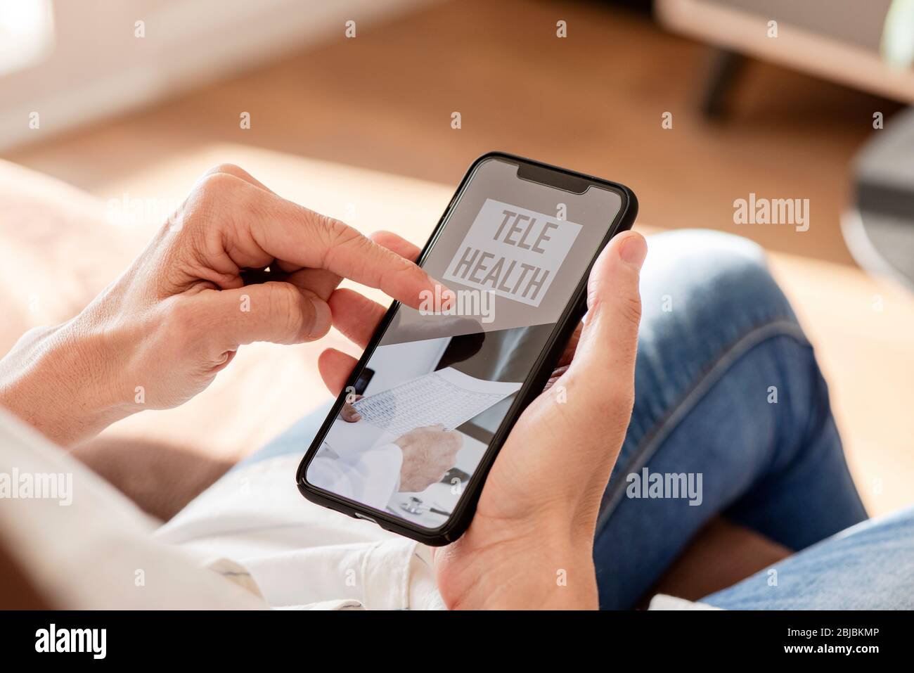 primo piano di un giovane caucasico, seduto comodamente in un divano, utilizzando il suo smartphone, con il testo di telesanità sul suo schermo Foto Stock