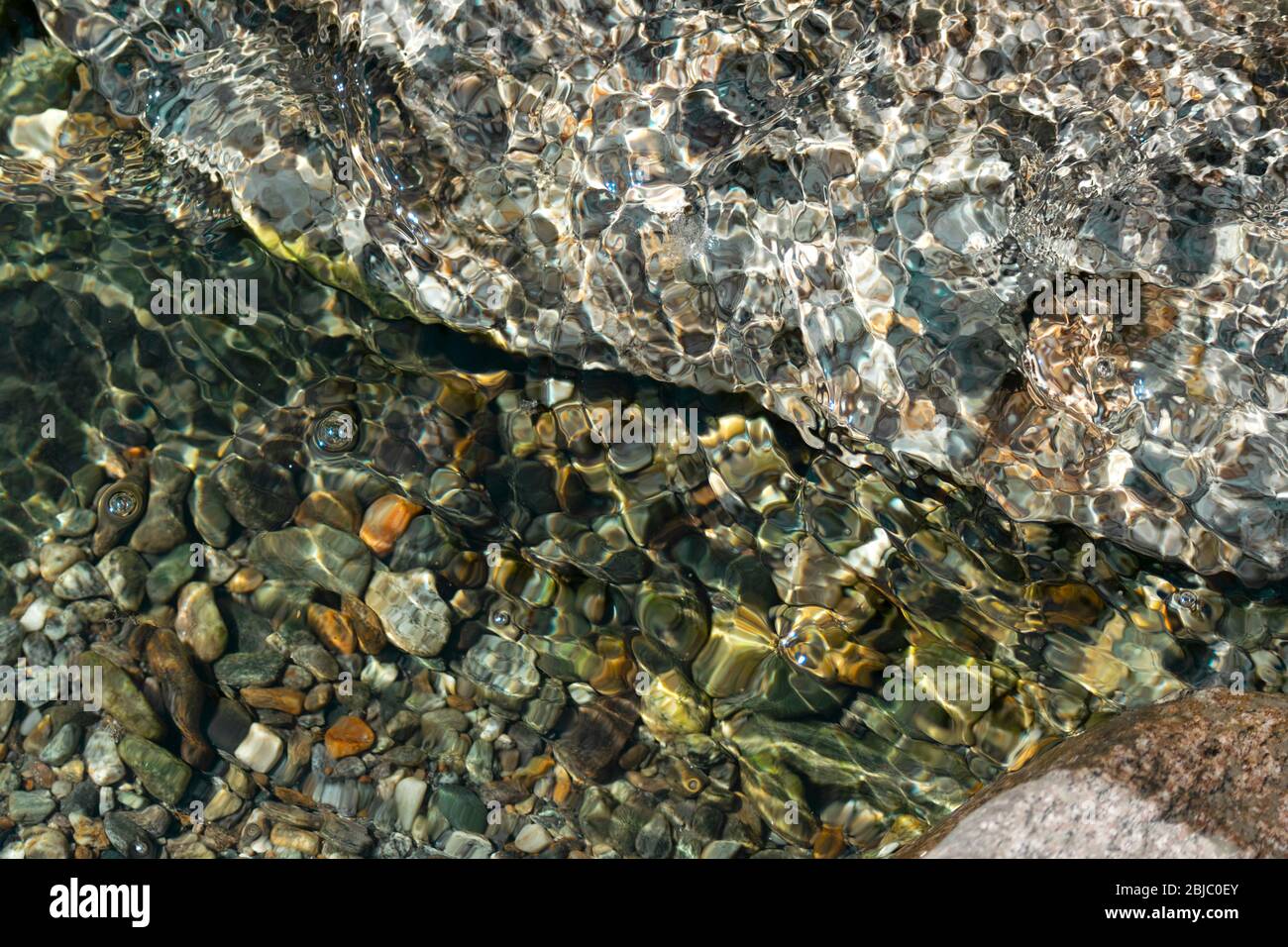 acque limpide e calme, con ciottoli colorati sott'acqua e una roccia, al mare, al fiume o al lago. Acqua trasparente. Foto Stock