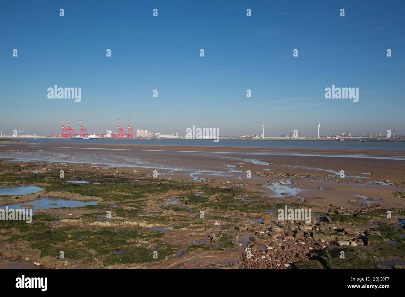 Città di Wallasey, Inghilterra. Nuova spiaggia di Brighton con il fiume Mersey e le gru rosse al Seaforth Container Terminal, sullo sfondo. Foto Stock