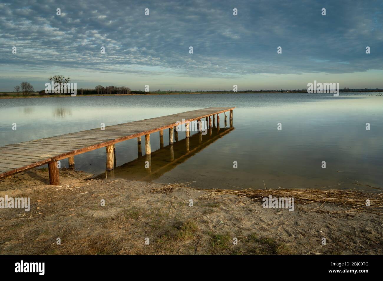 Molo in legno verso il lago calmo e nuvole su un cielo serale Foto Stock