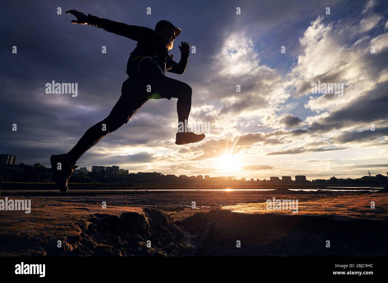 Uomo in silhouette jump correndo contro NUVOLOSO TRAMONTO cielo Foto Stock