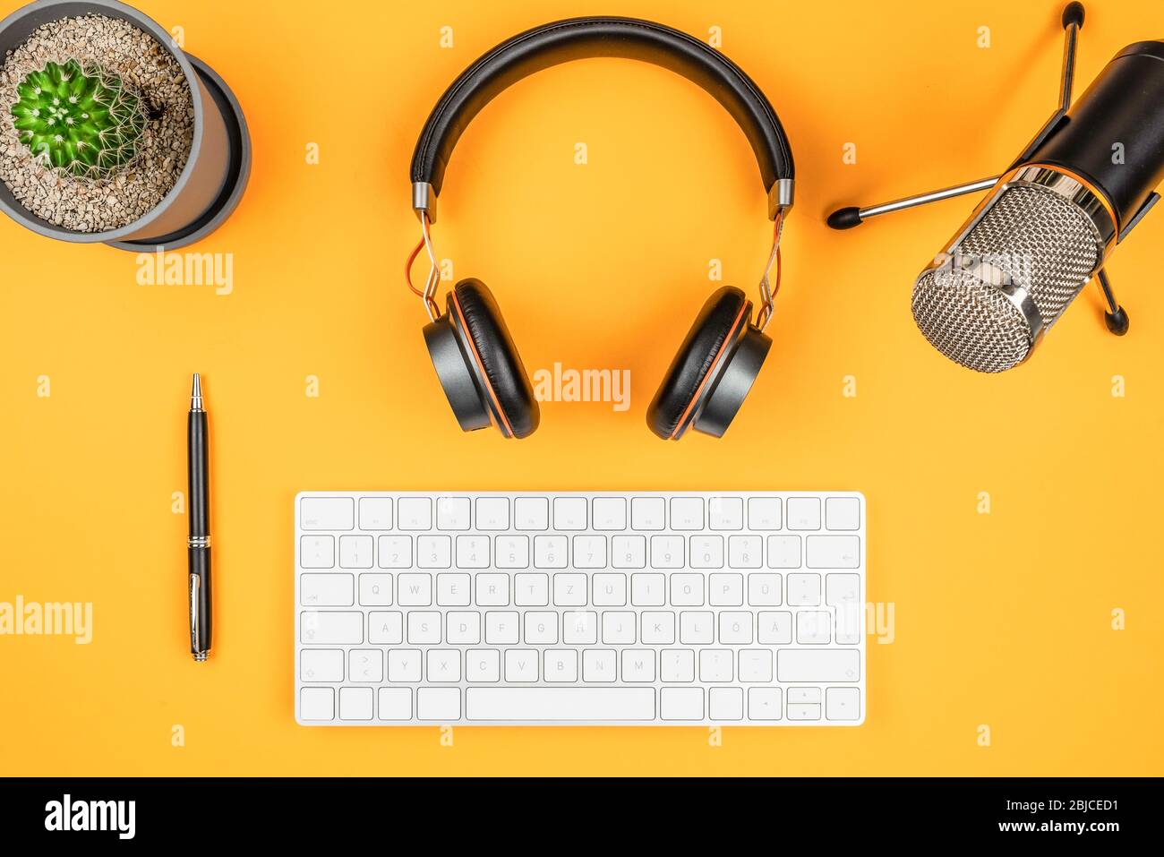concetto di podcasting e registrazione podcast, vista dall'alto di microfono, cuffie e tastiera del computer su scrivania arancione Foto Stock