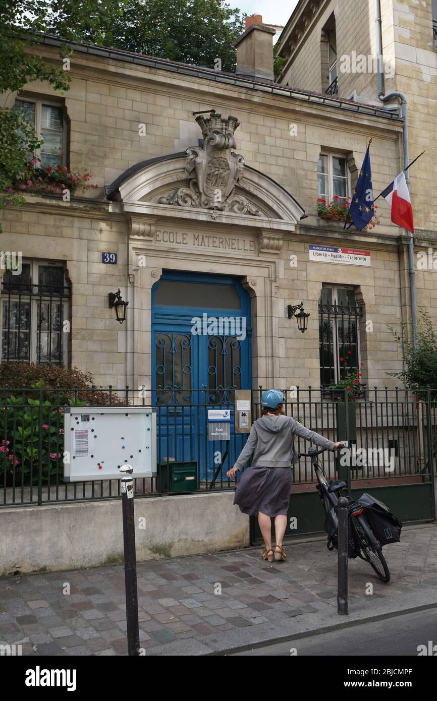 Lady con la sua bici di fronte a un ingresso della scuola pubblica francese, Parigi Foto Stock