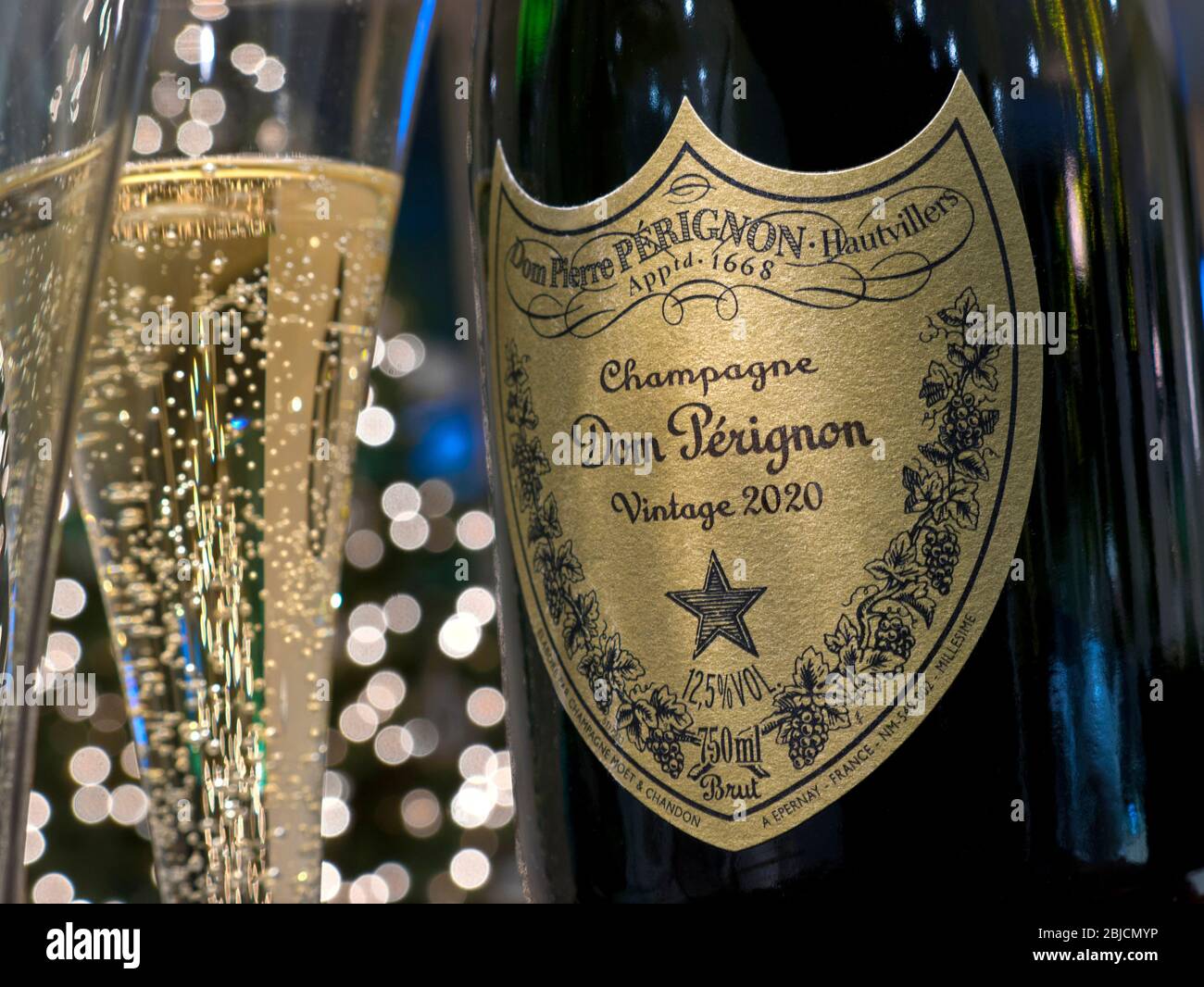 Dom Perignon bottiglia di champagne e bicchiere di champagne versato in atmosfera di festa con luci scintillanti in concept label di sfondo post-datato al 2020 Foto Stock
