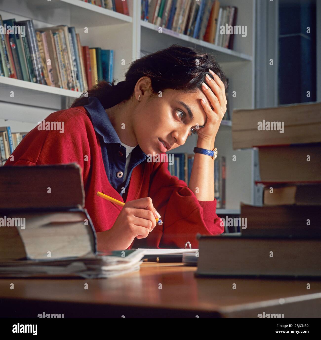 Ragazza studentesca asiatica 15 anni concentrandosi a studiare con attenzione per gli esami in biblioteca scolastica. Libri di esame e di riferimento sul tavolo della biblioteca scolastica Foto Stock