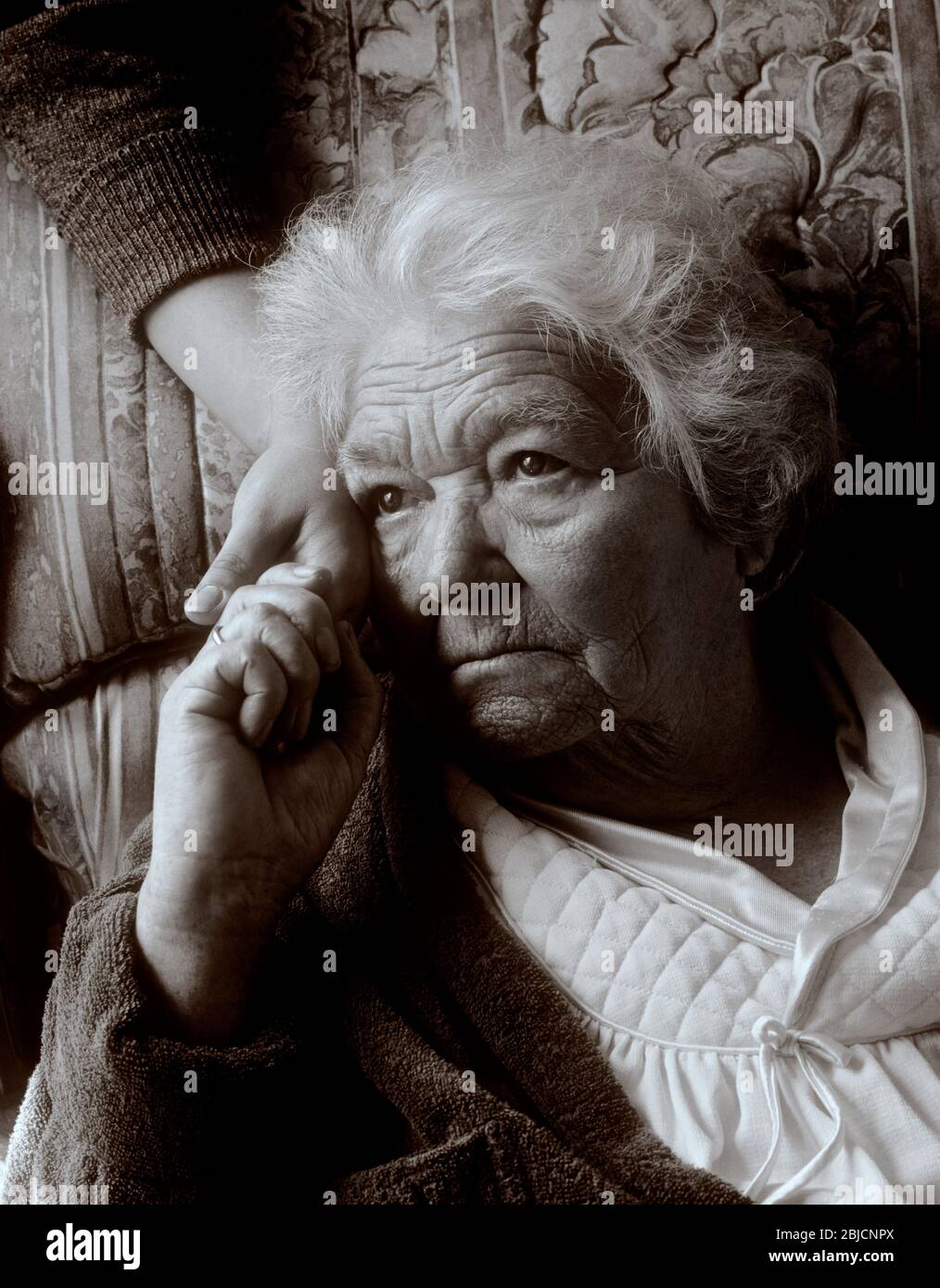 Cura della vecchiaia apprensiva anziana signora anni '90 tiene la mano confortante di caregiver in luce naturale interno ritratto verticale Foto Stock