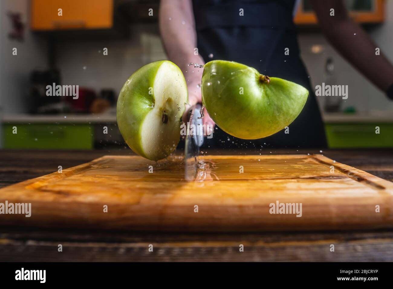 Chef che taglia una mela verde a metà con un grande coltello in movimento.  Spruzzi di acqua e succo volare in diverse direzioni e congelare in aria  Foto stock - Alamy