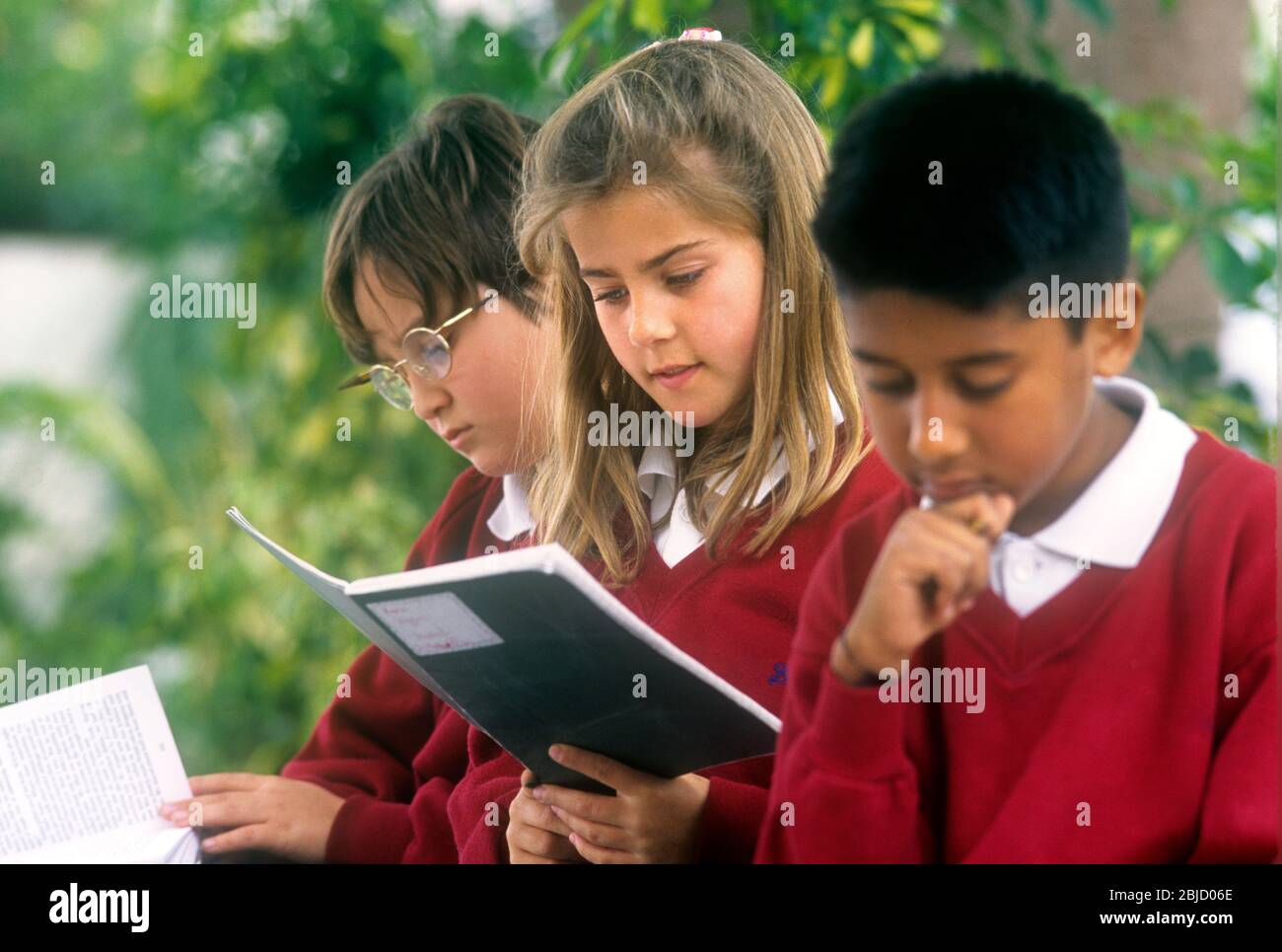 Gruppo di studenti studia attraente scuola junior 9-11 anni fuori in un ampio parco giochi con fogliame dietro Foto Stock