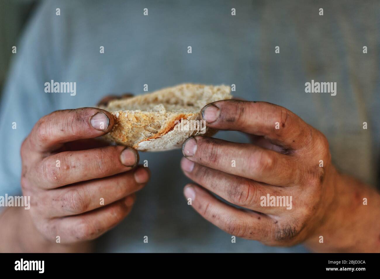 Pezzo di pane appena sfornato in mani sporche di un uomo duro. Concetto di guadagnare il vostro alimento quotidiano dal lavoro reale. Foto Stock