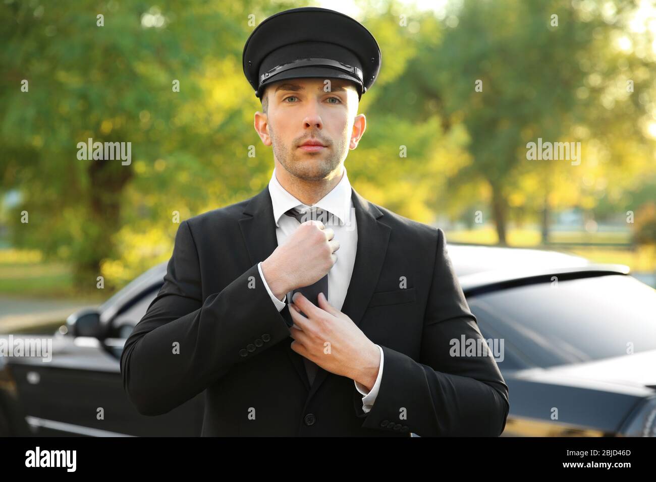 Giovane autista che regola cappello vicino auto di lusso sulla strada Foto  stock - Alamy