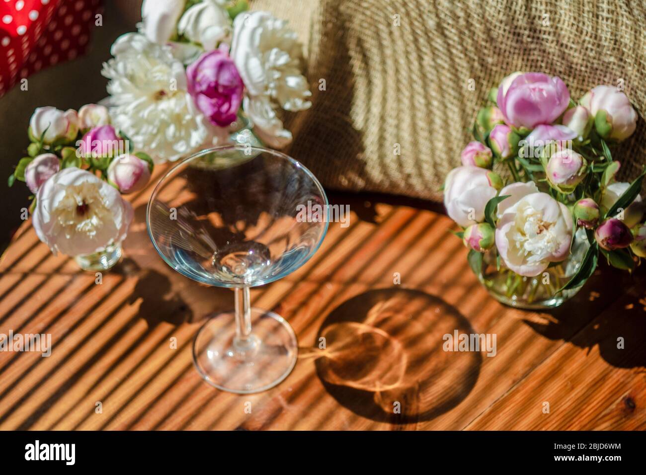 Festosa vita rustica con vetro vuoto vetro trasparente circondato da fiori bianchi su sfondo tessile su tavolo di legno. Ombra diagonale a righe di t Foto Stock