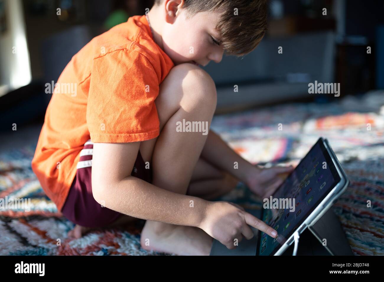 Ragazzo inginocchiato sul tappeto a casa con ipad tablet selezione app Foto Stock