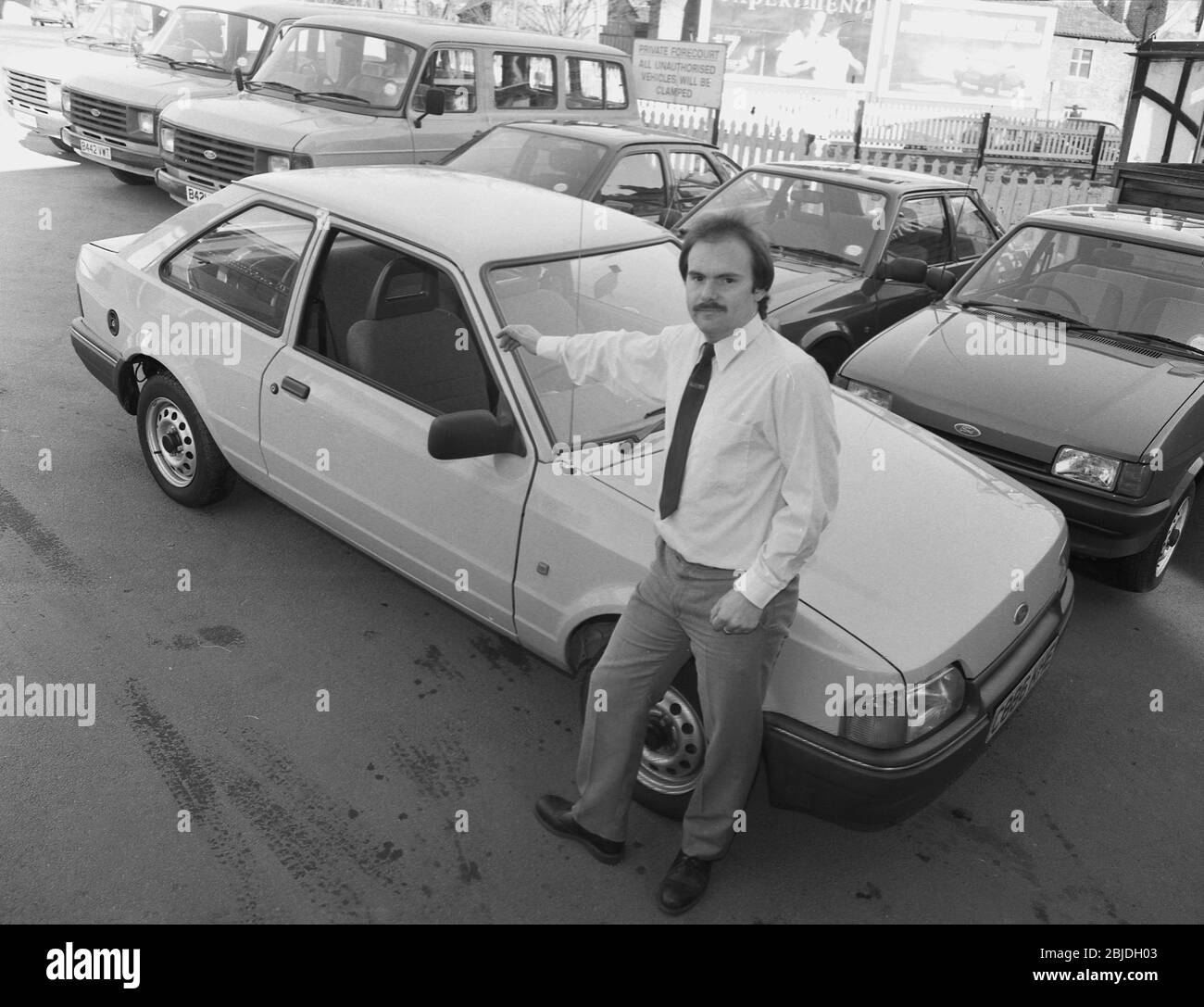 Anni '80, storico, un venditore di auto in piedi fuori in un precorpido da una nuova automobile, una Ford Escort due porte, Inghilterra, Regno Unito. Foto Stock