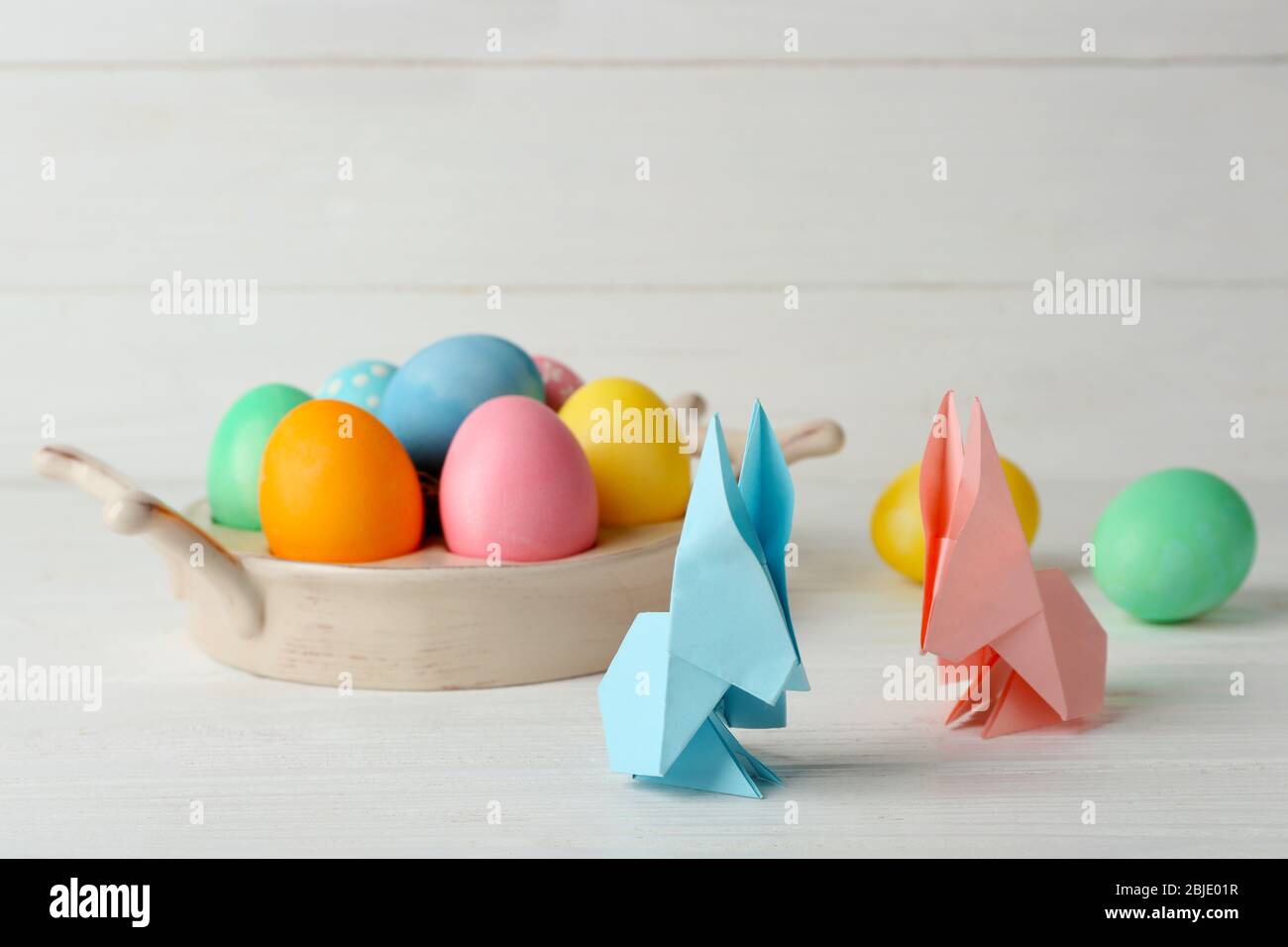 Conigli di Pasqua con uova colorate su tavolo di legno su sfondo chiaro Foto Stock