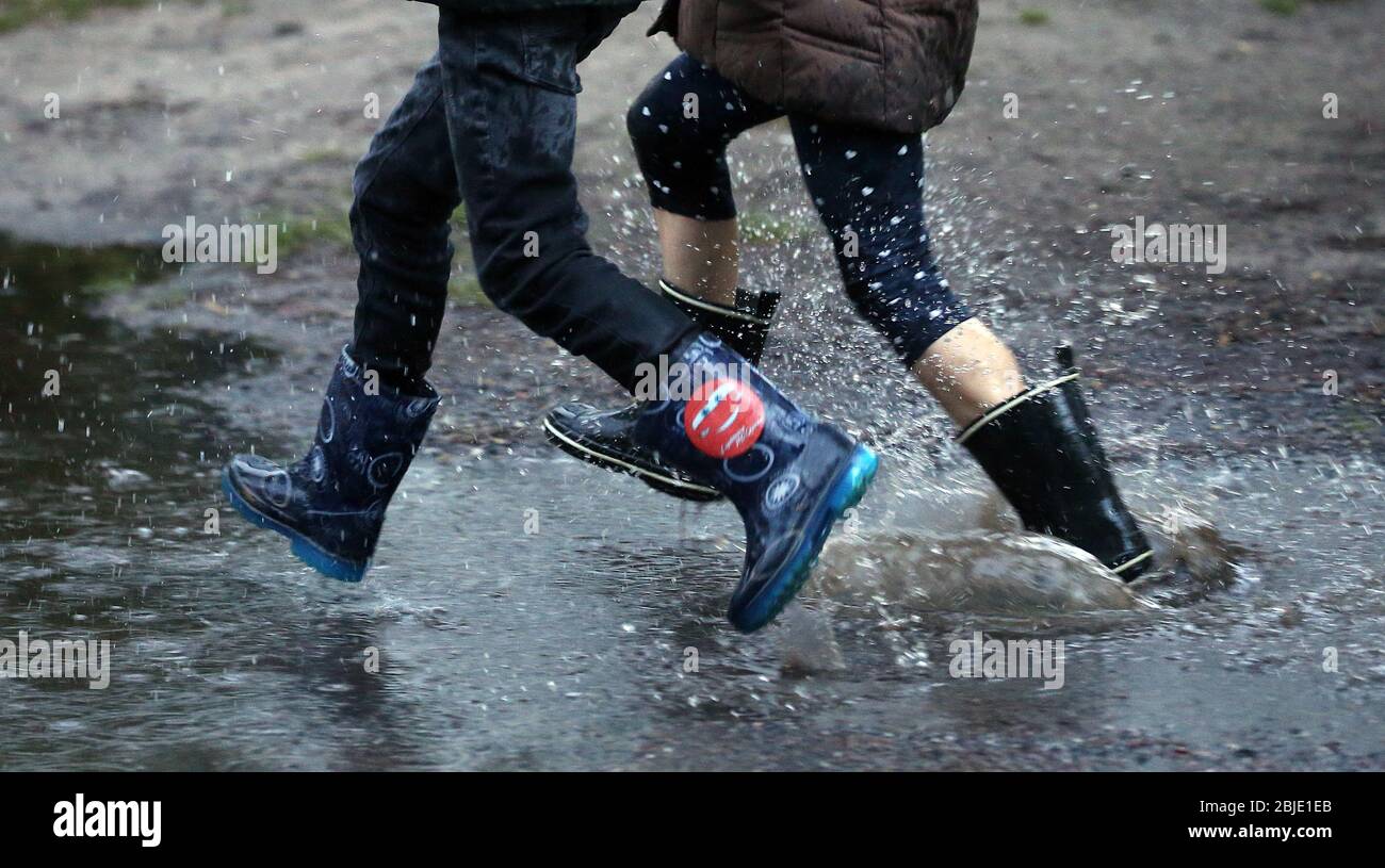 Berlino, Germania. 29 aprile 2020. I bambini del quartiere di Köpenick corrono con stivali di gomma attraverso grandi pozzanghere che si sono formate per le strade dopo forti docce a pioggia. Dopo settimane di siccità, la tanto attesa pioggia è caduta nel pomeriggio nella capitale. Secondo i meteorologi, le precipitazioni dovrebbero continuare nei prossimi giorni, con la diminuzione delle temperature. Credit: Wolfgang Kumm/dpa/Alamy Live News Foto Stock