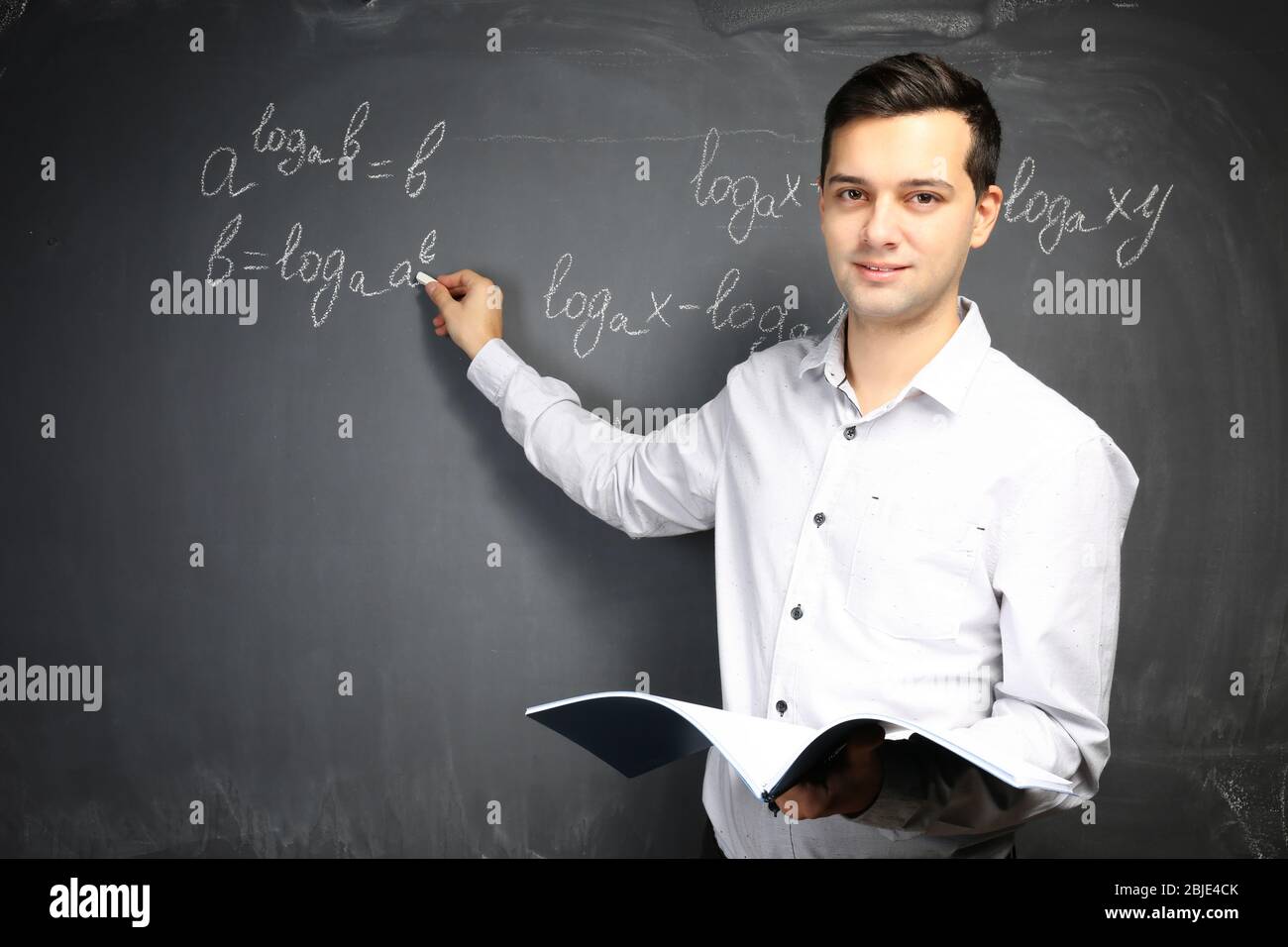Bel giovane insegnante scrivere formule matematiche sulla lavagna Foto Stock