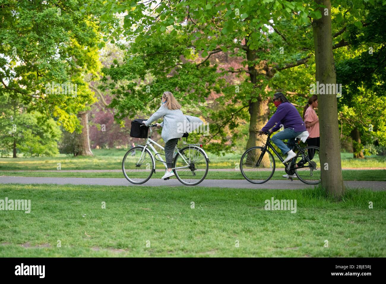 Due ciclisti che attraversano il parco con la bocca coperta contro il Covid-19, Londra, Lockdown Foto Stock