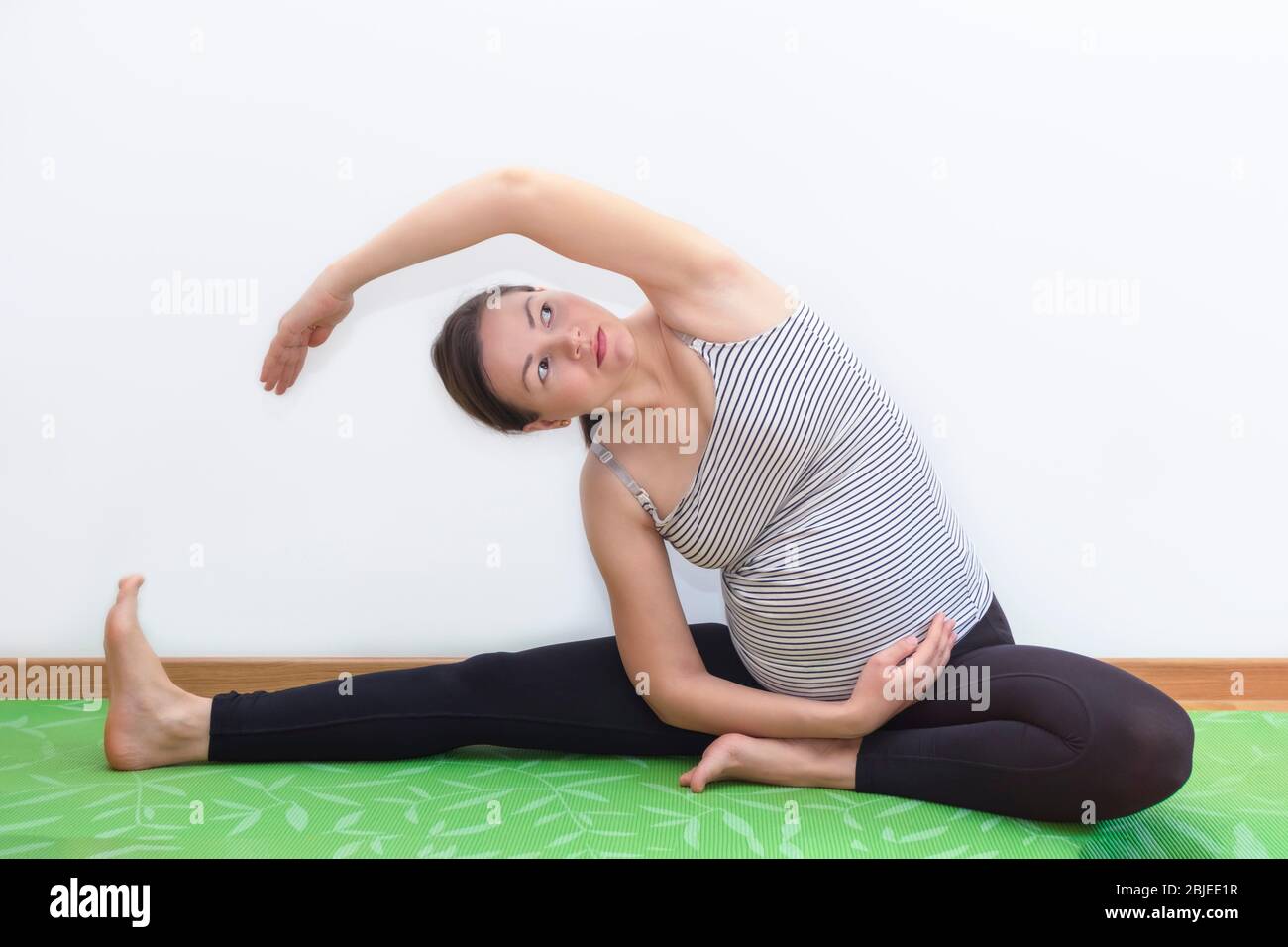 Giovane donna incinta in posizione di sidebend traing yoga prenatale a casa Foto Stock