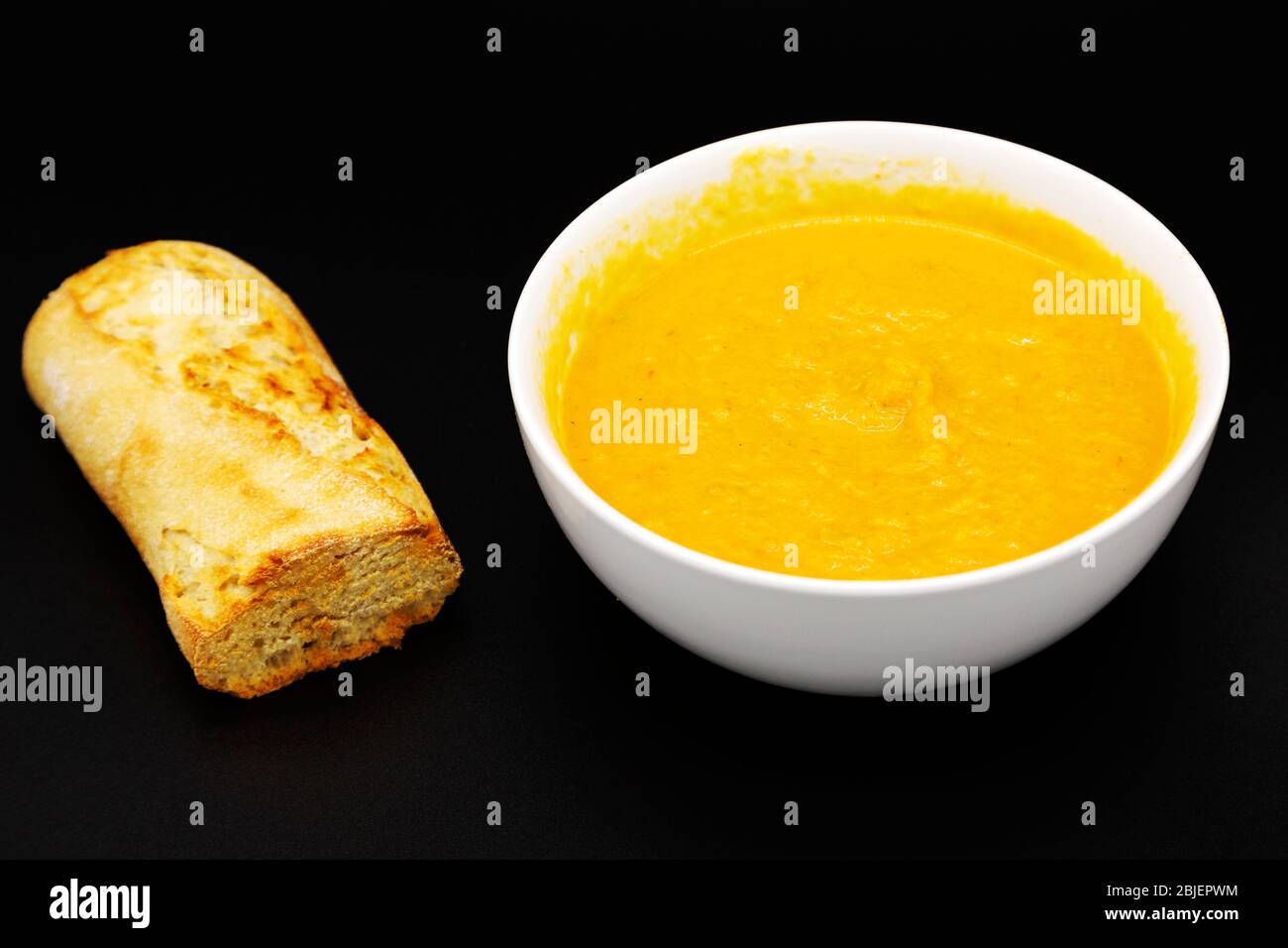 Una ciotola di zuppa di zucca alle butternut. La zuppa viene servita con metà baguette appena cotte. Foto Stock