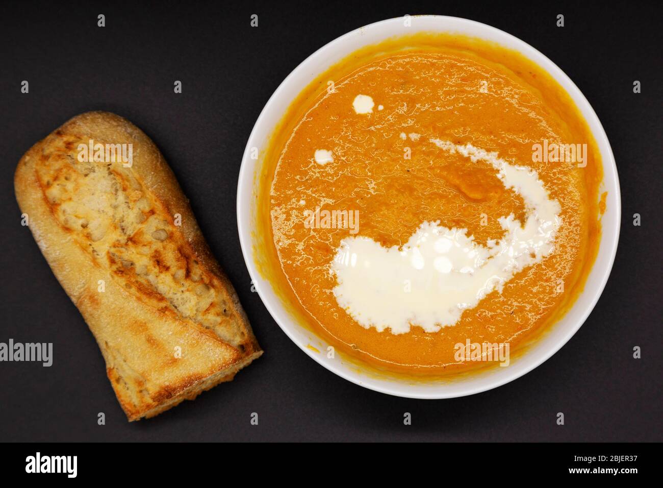 Una ciotola di zuppa di zucca alle butterne servita con un vortice di crema. La zuppa viene servita con metà baguette appena cotte. Foto Stock